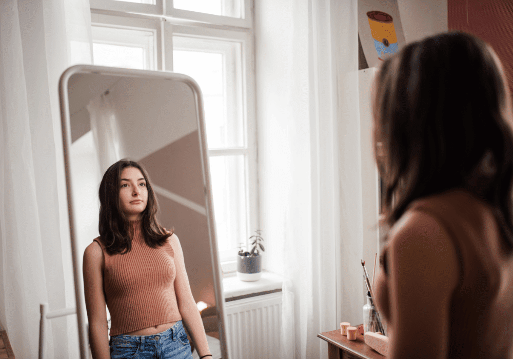 Person reflecting by window during eating disorder identity recovery journey toward authentic self